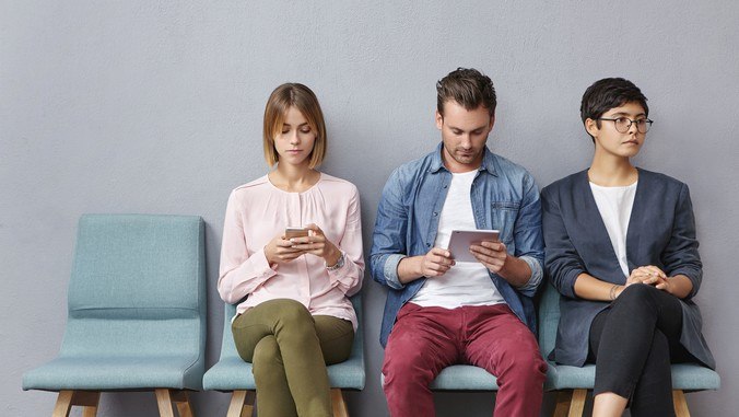 Zwei weibliche und ein männlicher Patient in einem Wartezimmer, die Smartphones und E-Reader nutzen