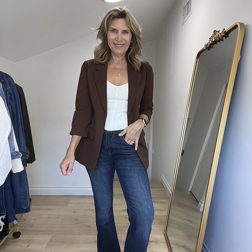 Woman wearing a brown blazer, white top, and dark jeans.