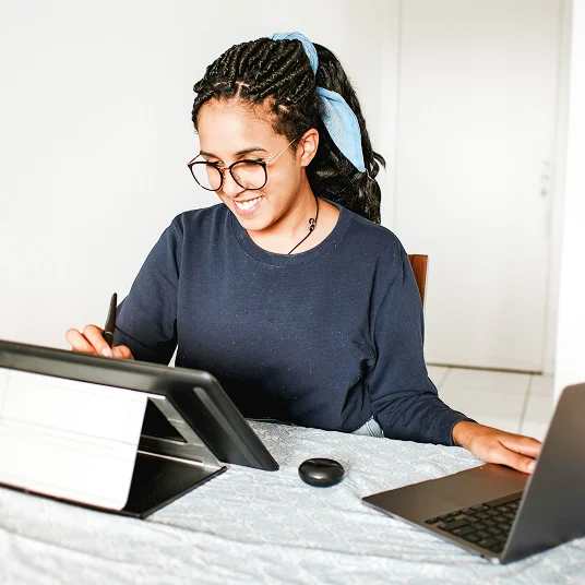 A women with curly hair and glasses working on two screens