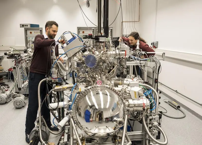 Two researchers work on a complex scientific apparatus in a laboratory filled with advanced equipment.