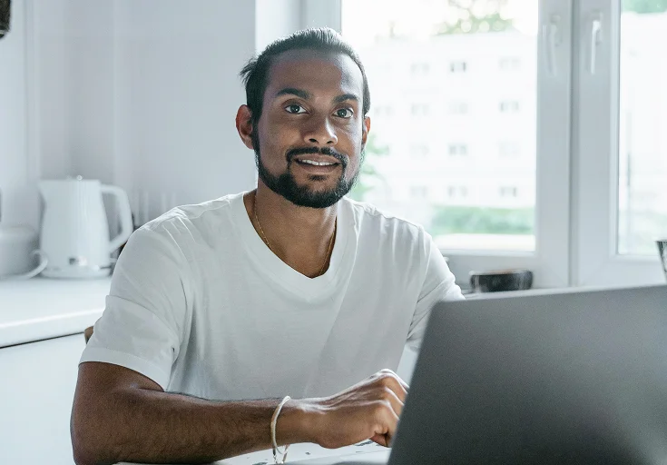 A male PoC sitting in front of a laptop smiling