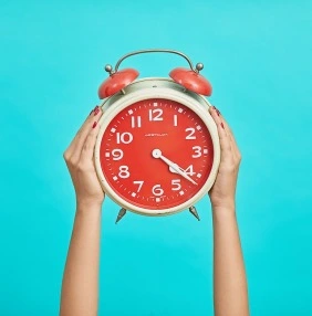 kid holding up a red alarm clock