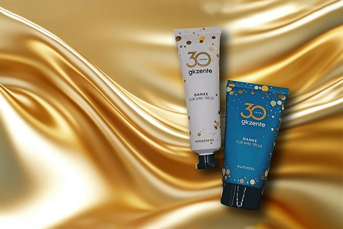 weiße Handcremetube und türkise Duschgeltube auf goldenem Hintergrund