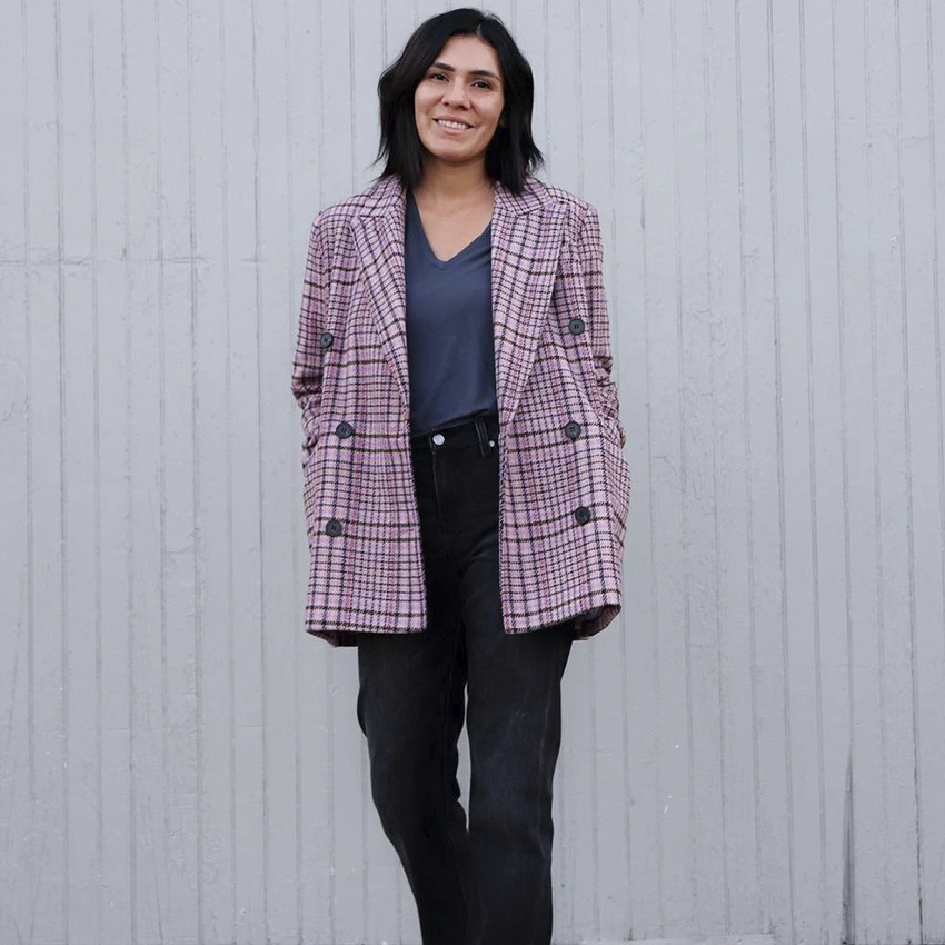 Woman wearing a pink plaid blazer, gray T-shirt, and black jeans.