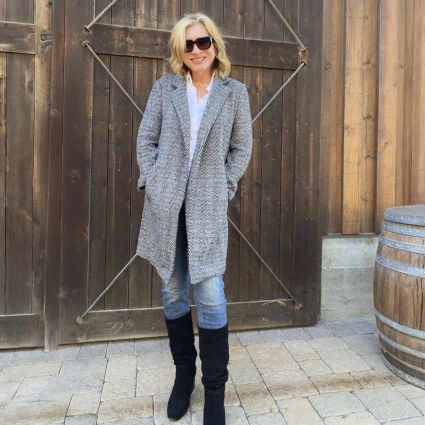 Woman in a gray herringbone blazer, jeans, and black boots.