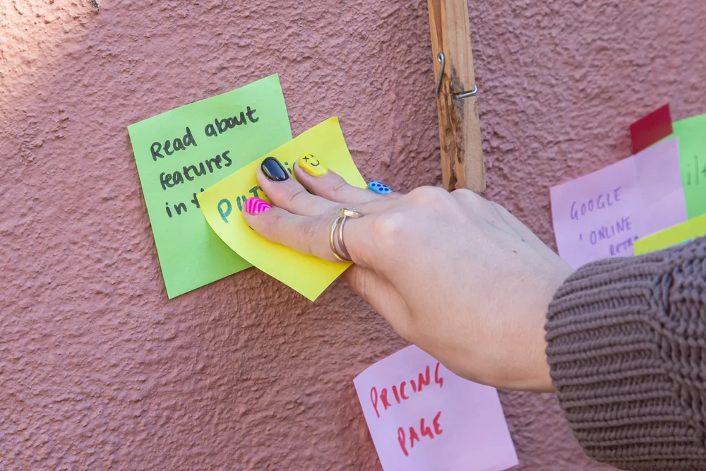 A hand with painted nails putting stickies on a wall