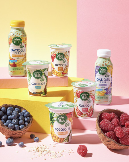 kubeczki i butelki deseru OATJOGU z linii produkt&oacute;w GoVege, w otoczeniu świeżych owoc&oacute;w; bor&oacute;wek i malin