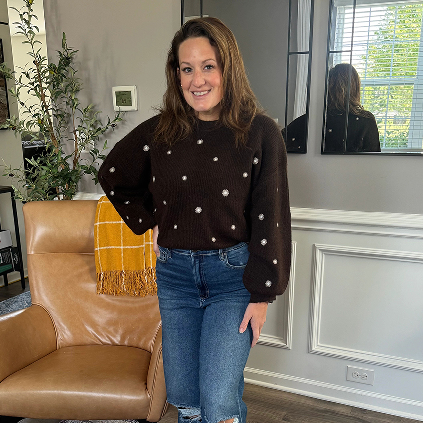 Woman wearing a brown blazer, white top, and dark jeans.