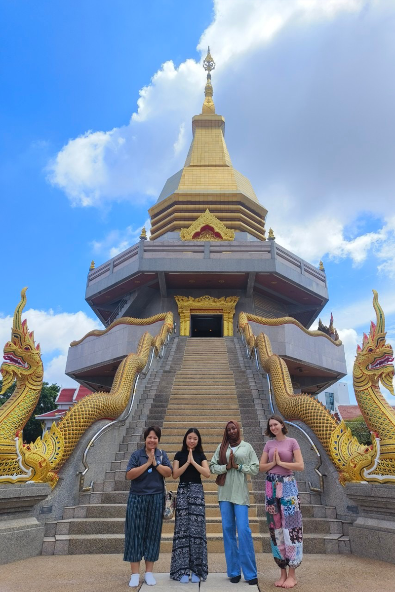 Three students with their Resident Director in front of a traditional Thai Wat in Thailand.