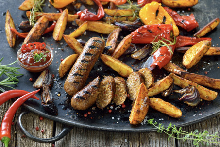 upieczone, wegańskie kiełbaski, ułożone na czarnym talerzu, w otoczeniu pieczonych warzyw.