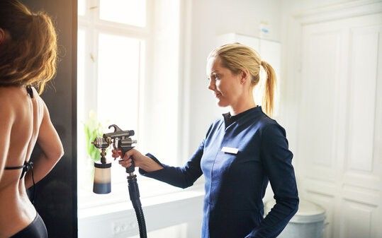 Profissional passando spray de bronzeamento Imagem de uma profissional passando spray de bronzeamento