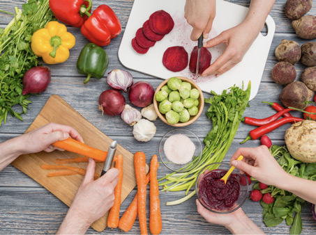 dłonie krojące, mieszające i obierające r&oacute;żne rodzaje warzyw, kt&oacute;re są ważnym elementem diety wegan