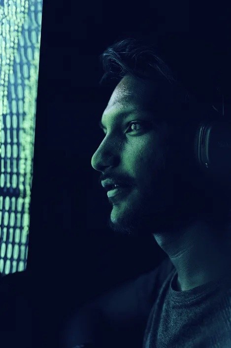 A male with headphones looking on a big green shiny screen with numbers