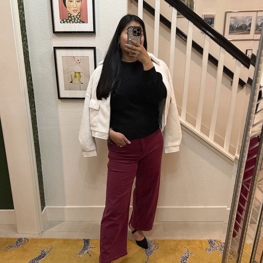 Woman takes a mirror selfie in red pants, black top, and white jacket.