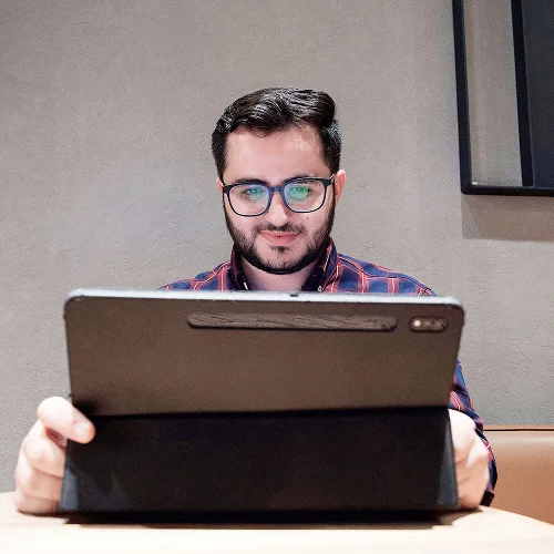 A young man with glasses smiling in front of a tablet