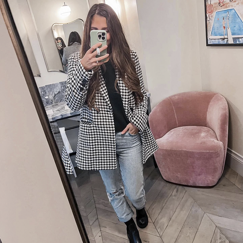 Woman takes a mirror selfie in a houndstooth blazer and ripped jeans.