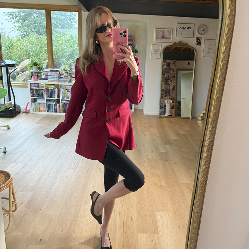 Woman wearing a brown blazer, white top, and dark jeans.
