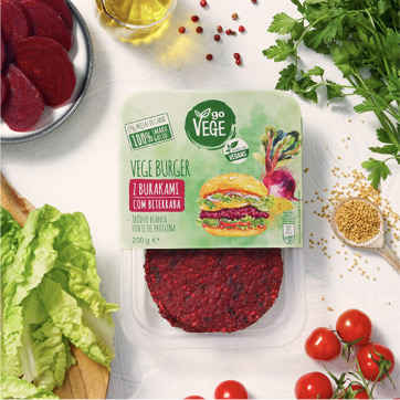 VEGE BURGER z burakami Go Vege, wokoło świeże liście sałaty, pietruszki, pomidorki koktajlowe, plastry buraka i rozsypane nasiona kolendry.