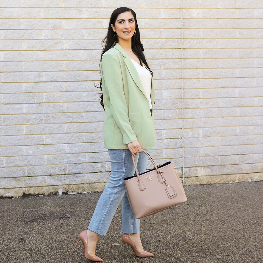 Woman in a mint green blazer and jeans carrying a blush handbag.
