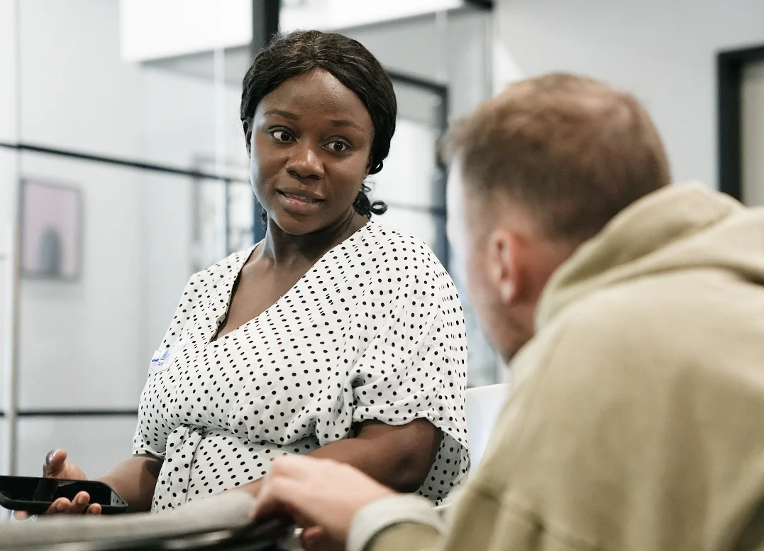 A female PoC talking to a blond guy