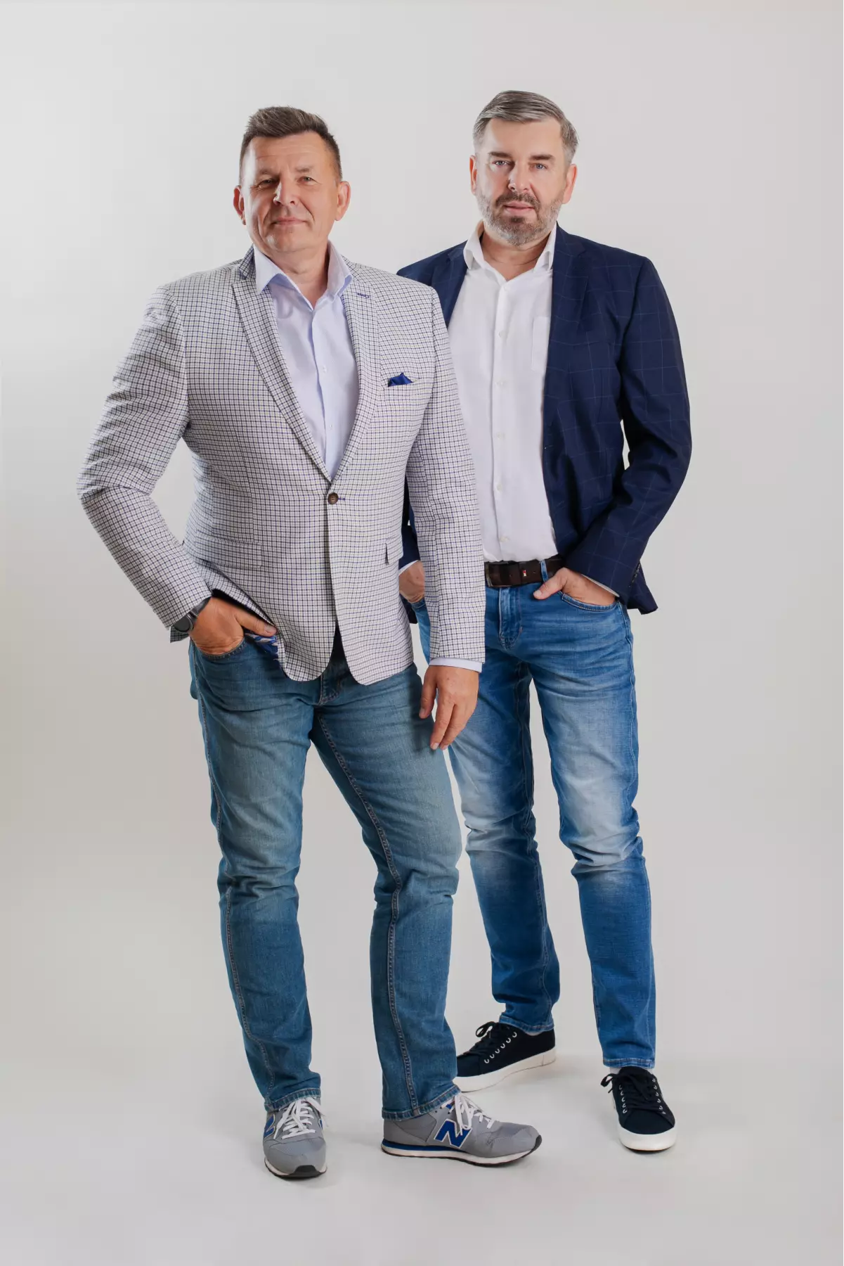 Dwóch przedsiębiorców w eleganckich marynarkach i jeansach, stojących obok siebie.