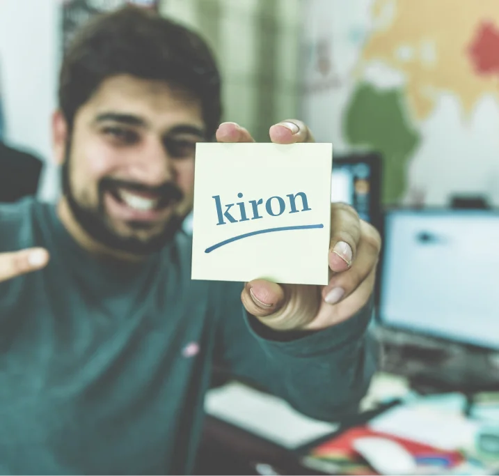 A young man holding up a sticky note showing the kiron logo