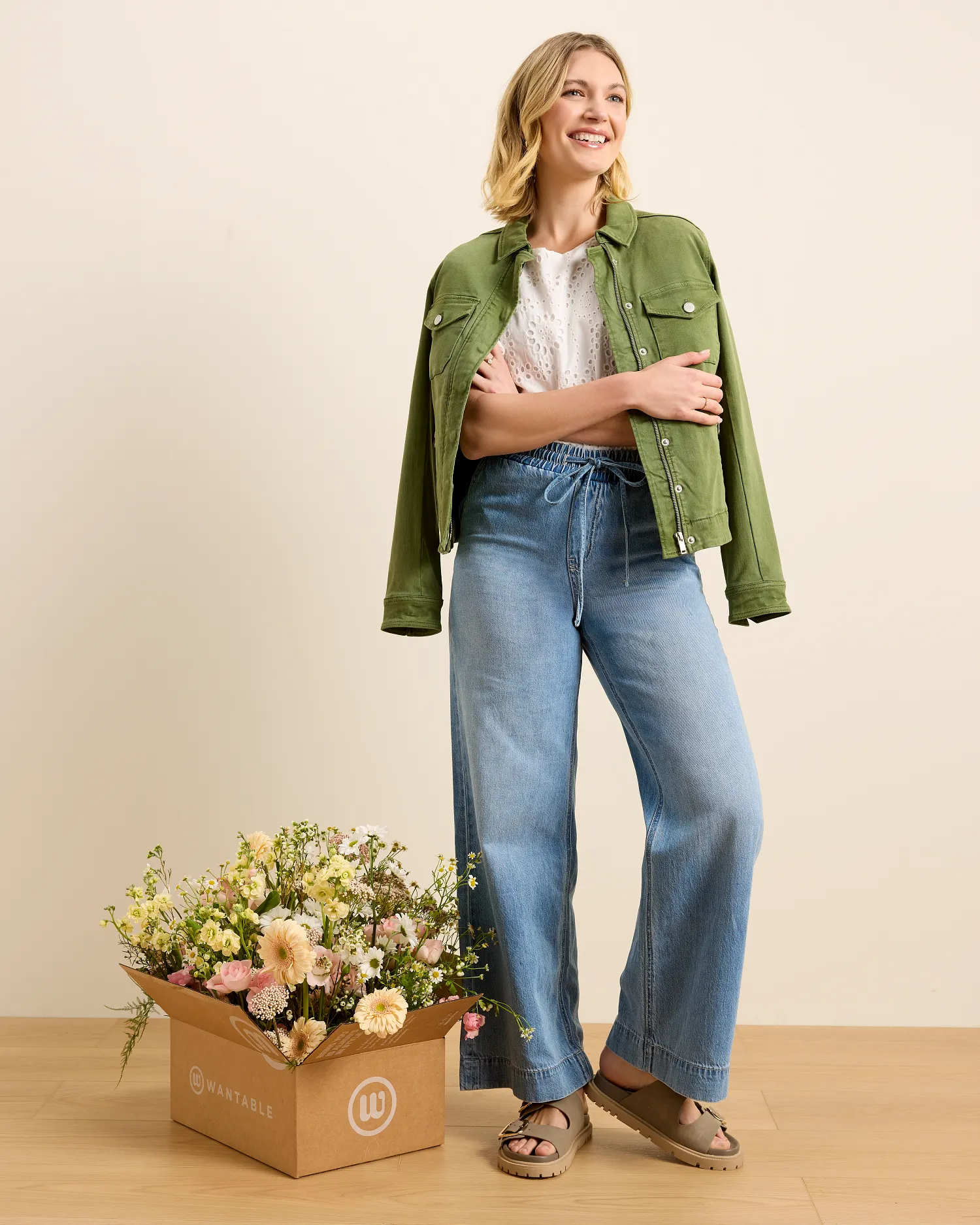 Green floral sleeveless dress draped over a modern chair and styled with a brown belt, light blue blazer, and sunglasses on the seat. The outfit is arranged as a complete warm weather look against a neutral background to showcase the styling pieces together.