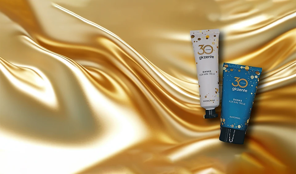 weiße Handcremetube und türkise Duschgeltube auf goldenem Hintergrund